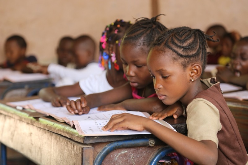 Deux fillettes penchées sur leur cahier de lecture, à leur pupitre.